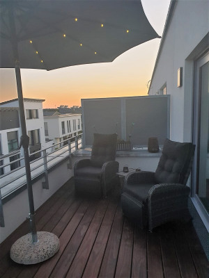 Eine Terrasse mit zwei Sesseln, einem Sonnenschirm und einer abendlichen Stadtansicht im Hintergrund.