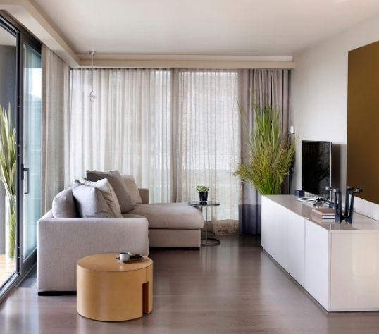 Modernes Wohnzimmer mit Sofa, Couchtisch, Fernseher und großen Fenstern.