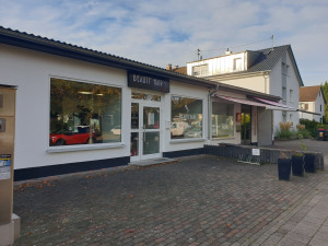 Ein kleines Geschäft mit großen Fenstern und einem Schild, das "Buchhandlung" zeigt, steht an einer ruhigen Straße.