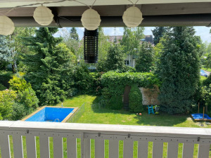 Balkon mit Blick auf einen Pool, grünen Garten und Bäume, dekoriert mit weißen Papierlaternen.